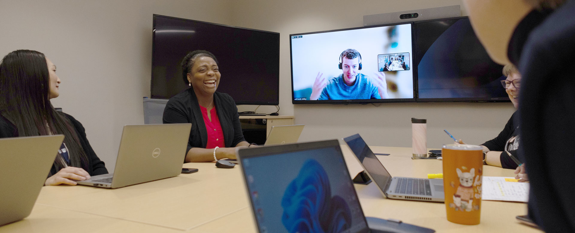 A small group of staff in a boardroom connecting on a Zoom call with a colleague